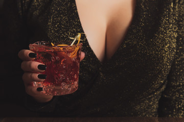 Girl in evening dress with big breast holds an alcohol cocktail in a hand. Hot woman at the party. Temptation in a bar with sexy neckline. Consummation concept photo. © Alexander