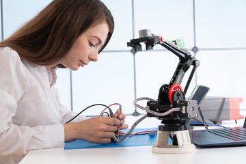 A young woman writes an algorithm for the robot arm. Science Research Laboratory for Robotic Arm...