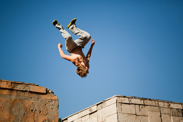 Plakat Young man jumping and practicing parkour between two building outside on clear summer day