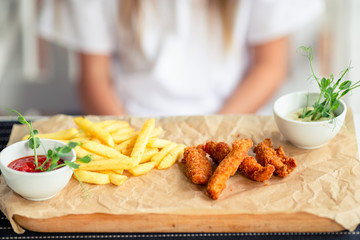 Closeup crispy potato fries with two dipping sauce and fresh chicken fingers served on Rustic wooden plate