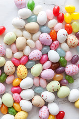 Happy Easter concept. Preparation for holiday. Easter candy chocolate eggs and jellybean sweets on trendy gray marble background. Simple minimalism flat lay top view copy space.