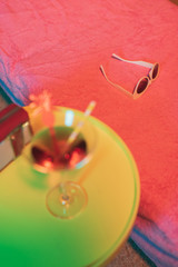 Sunglasses on sunbed with yellow table and cocktail drink and portable radio next to it.