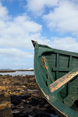 Top of green wooden fishing boat wreck stranded on beach with reef rocks, tide out .