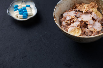 Bowl of granola with yogurt and banana and sports supplements on dark stone background. Close up. Copy space. 