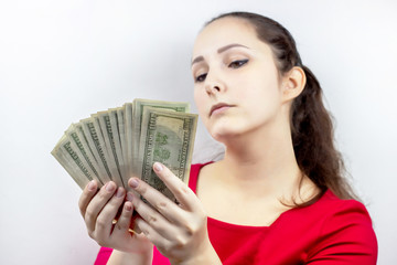 Pretty young caucasian brunette woman in casual red dress holding american dollars in her hands. Finance and money, earnings and savings, salary and income concept.