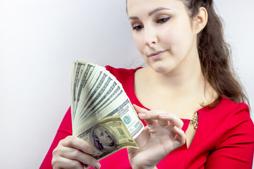 Pretty young caucasian brunette woman in casual red dress holding american dollars in her hands. Finance and money, earnings and savings, salary and income concept.