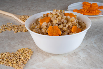 Fototapeta premium Spelt porridge in a white bowl and decorated with an asterisk carrot, diet food.