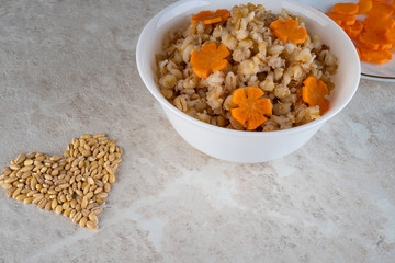 Spelt porridge in a white bowl and decorated with an asterisk carrot, diet food.
