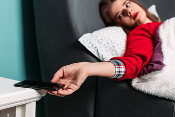 Girl waking up in the morning, taking her phone from the nightstand.