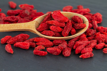 goji berries close up dried red berry in wooden spoon on grey slate plate