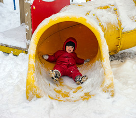 Little boy on the playground in winter day rides the slide