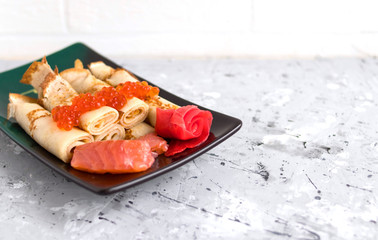pancakes twisted into a tube with red fish, red caviar and ginger on a concrete background