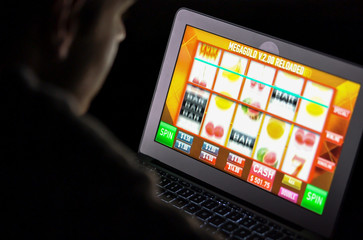 Gambling addicted man with glasses in front of online casino slot machine on laptop computer at night - loosing his money. Dramatic low light grain shot.