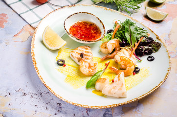 Closeup of grilled shrimp with red chili pepper sauce, vegetables at a table background.