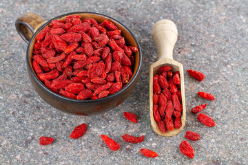 Cup and wooden spoon with dried red goji berries on gray stone background. Top view