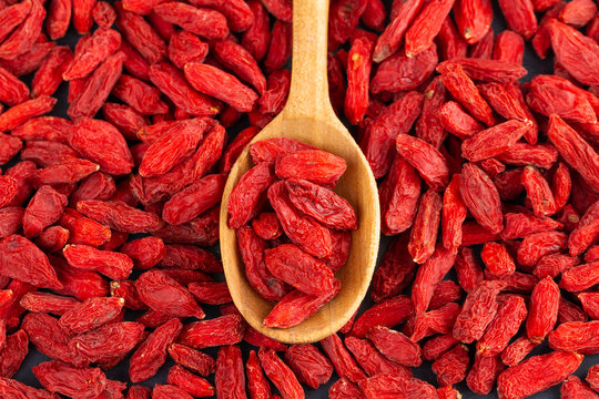 Spoon with Goji berries over red goji background. Healthy food concept.