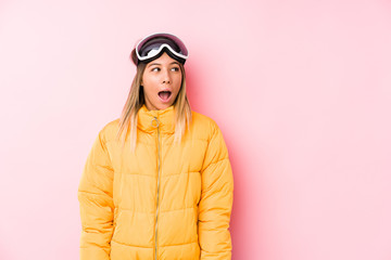 Young caucasian woman wearing a ski clothes in a pink background being shocked because of something she has seen.