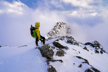 Naklejka na ściany i meble Alpinist overlooking winter alpine like moutain landscape of High Tatras, Slovakia. Climber in winter mountains on snow and rocky peaks.