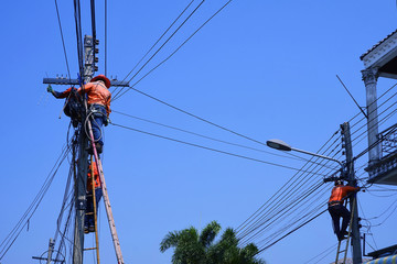 Fototapeta na wymiar Low angle view of technicians group on wooden ladder are working to install telephone wires on electric power pole against blue sky background, technology and development concept