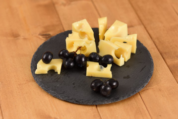 Cheese end black grapes on a slate plate on the wooden table
