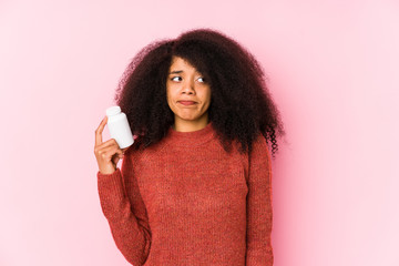 Young afro woman holding a vitamins isolated Young afro woman holding a vitaminsconfused, feels...