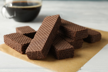 Craft paper with wafers and cup of coffee on white wooden background, close up