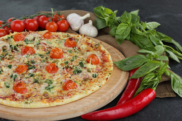 Italian concept, Italian cuisine. Pizza on a black background with fresh vegetables and herbs. Rustic.