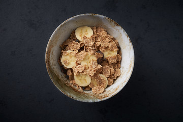 Bowl of granola with banana. Concept for a tasty and healthy meal. Dark stone background. Close up. Top view. Copy space. 