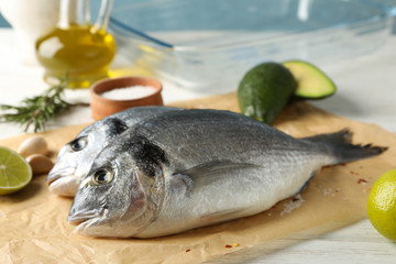 Baking paper with Dorado fishes and cooking ingredients on wooden background, close up