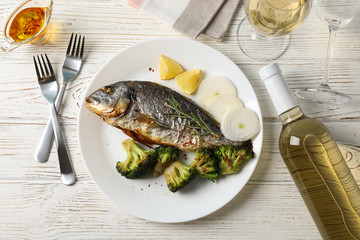 Plate with fried Dorado fish on garnished wooden background, top view
