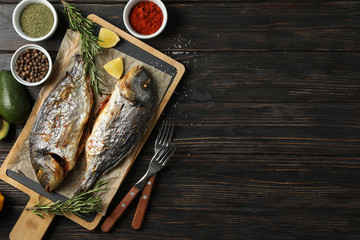 Cutting board with fried Dorado fishes and spice ingredients on wooden background, top view