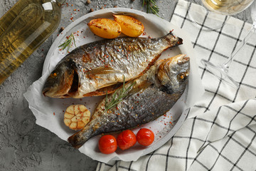 Plate with baked Dorado on garnished grey background, top view