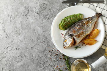 Plate with baked Dorado on garnished grey background, top view