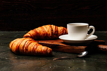 Tasty croissants and coffee in white cup on a dark background, side view