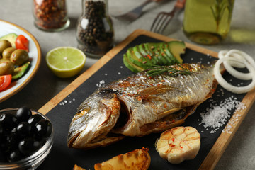 Cutting board with Dorado on garnished grey background, close up