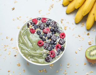 Green detox smoothie bowl with kiwi, bananas, granola and frozen berries. Healthy Breakfast, detox concept.