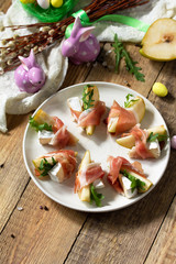 Festive snacks. Pear appetizer with jamon, arugula and brie cheese on a rustic wooden table. Copy space.