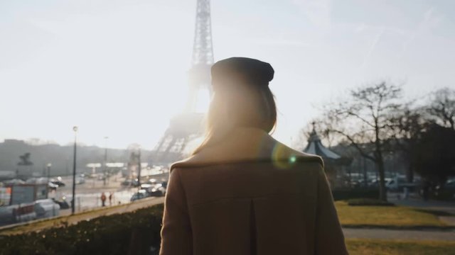 Camera follows happy relaxed beautiful woman walking along backlit sunny autumn Eiffel Tower in Paris slow motion.