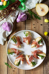 Festive snacks. Pear appetizer with jamon, arugula and brie cheese on a rustic wooden table. Top view flat lay background. Copy space.