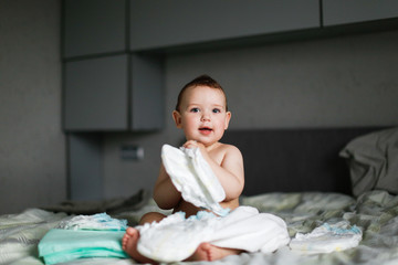 Cute chubby baby sitting with disposable diapers - obrazy, fototapety, plakaty