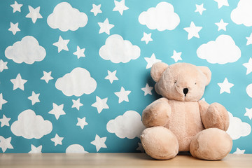 Teddy bear on wooden table near wall with painted blue sky, space for text. Baby room interior