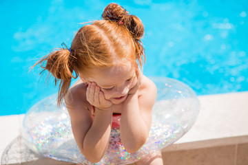 portrait of a little red-haired girl with funny tails on a transparent swimming circle