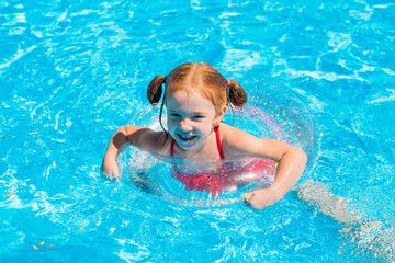 little redhead girl swims on a transparent swimming circle