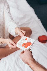 cropped view of couple with greeting card and gift box for valentines day on bed