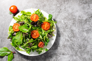 Green salad mix with cherry tomatoes on dark concrete background with copy space for your design. Healthy food concept.