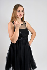 A photo of a pretty smiling girl with long hair and excellent make-up in a black dress is standing in various poses in the studio. Universal concept vertical woman portrait on a white background.