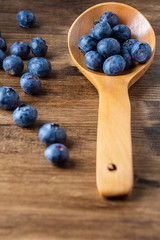 Top view of blue cranberries in a wooden spoon on dark wooden board with selective focus on vertical and copy space