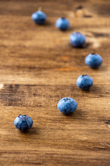 Top view of seven blue blueberries, the first one focused, the others in bokeh, on dark wooden board in vertical and copy space