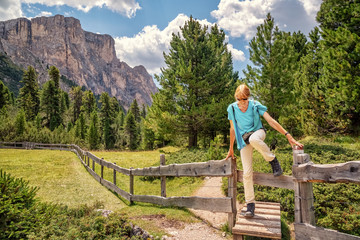 Fototapeta na wymiar Female hiker is climbing over a cattle fence on Col Raiser Alp in Val Gardena, Dolomite Alps in South Tyrol, Italy