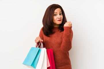 Middle age latin woman holding a shopping bags isolated showing fist to camera, aggressive facial expression.